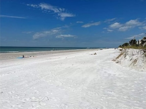 Uma extensa praia de areia com céu claro e mar calmo.