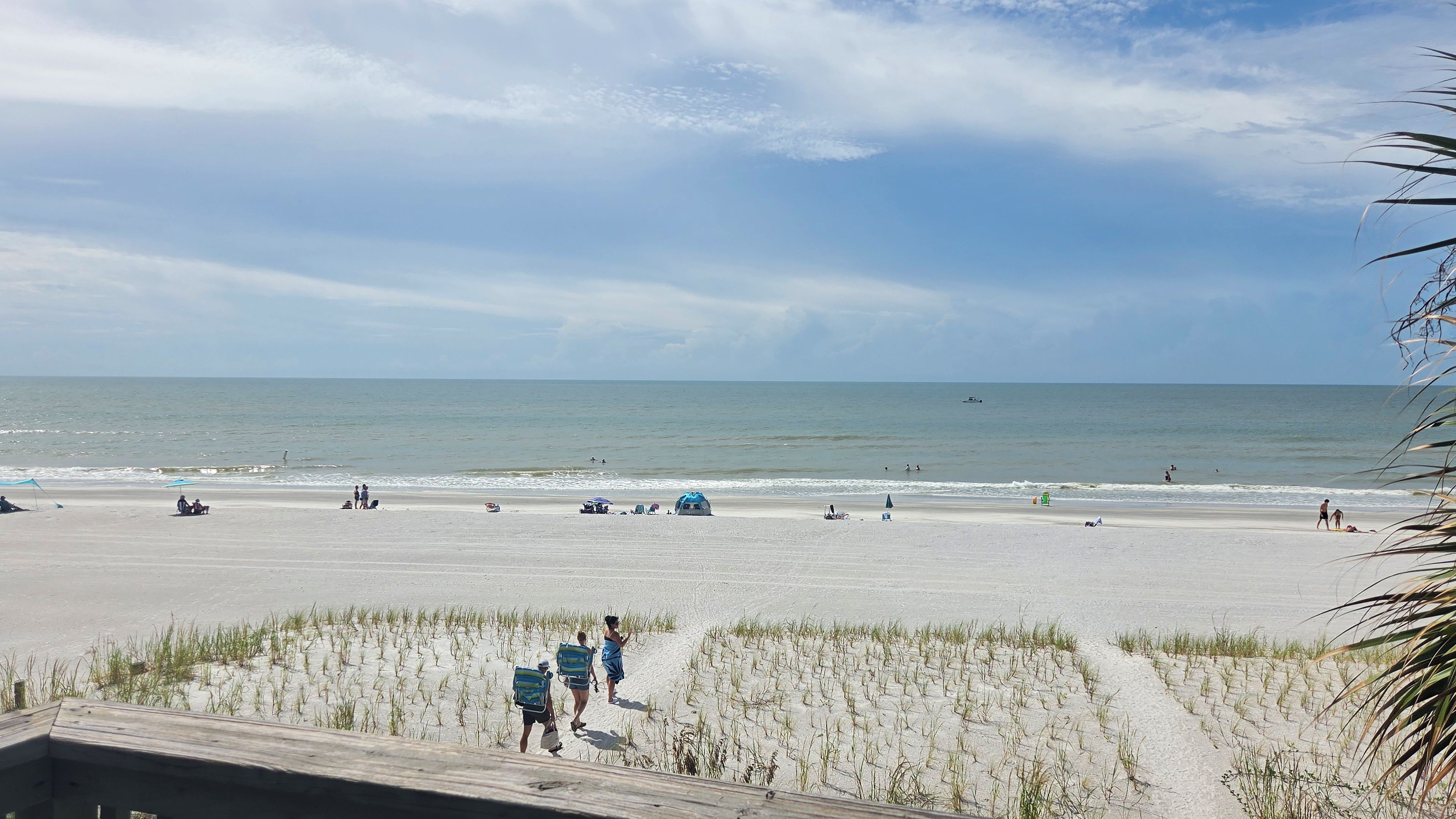 Une plage avec une promenade en bois qui mène au rivage, un ciel dégagé et une mer calme.