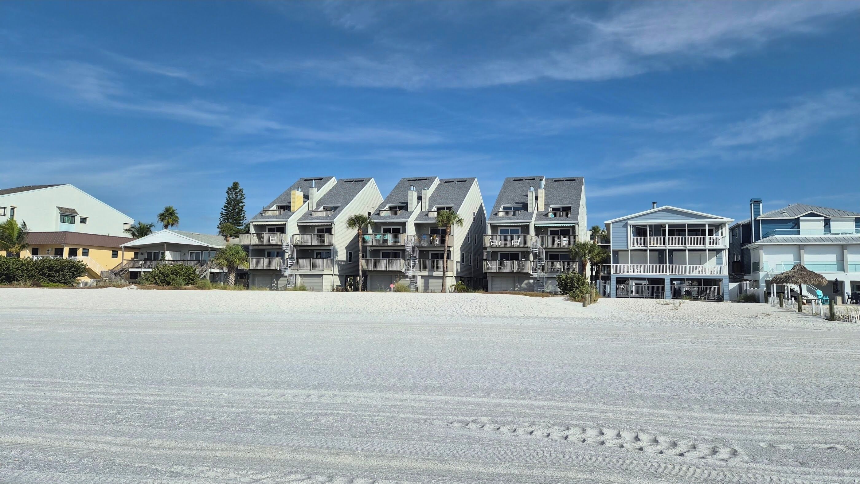 A beachfront property with multiple-story buildings, balconies, and a sandy beach in the foreground.