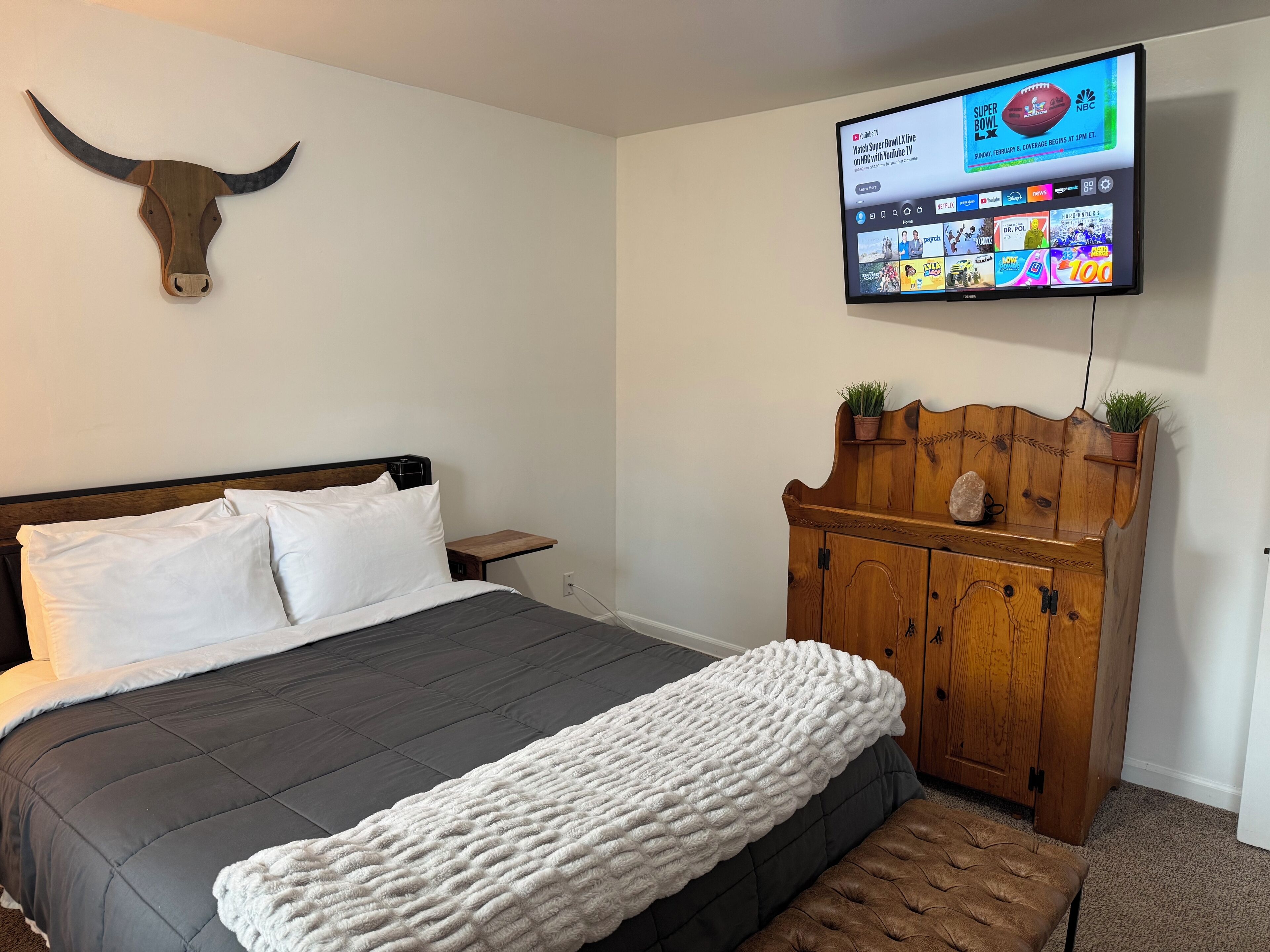 A bedroom with a bed, a wooden headboard, a mounted TV, and a wall-mounted wooden headboard with plants.