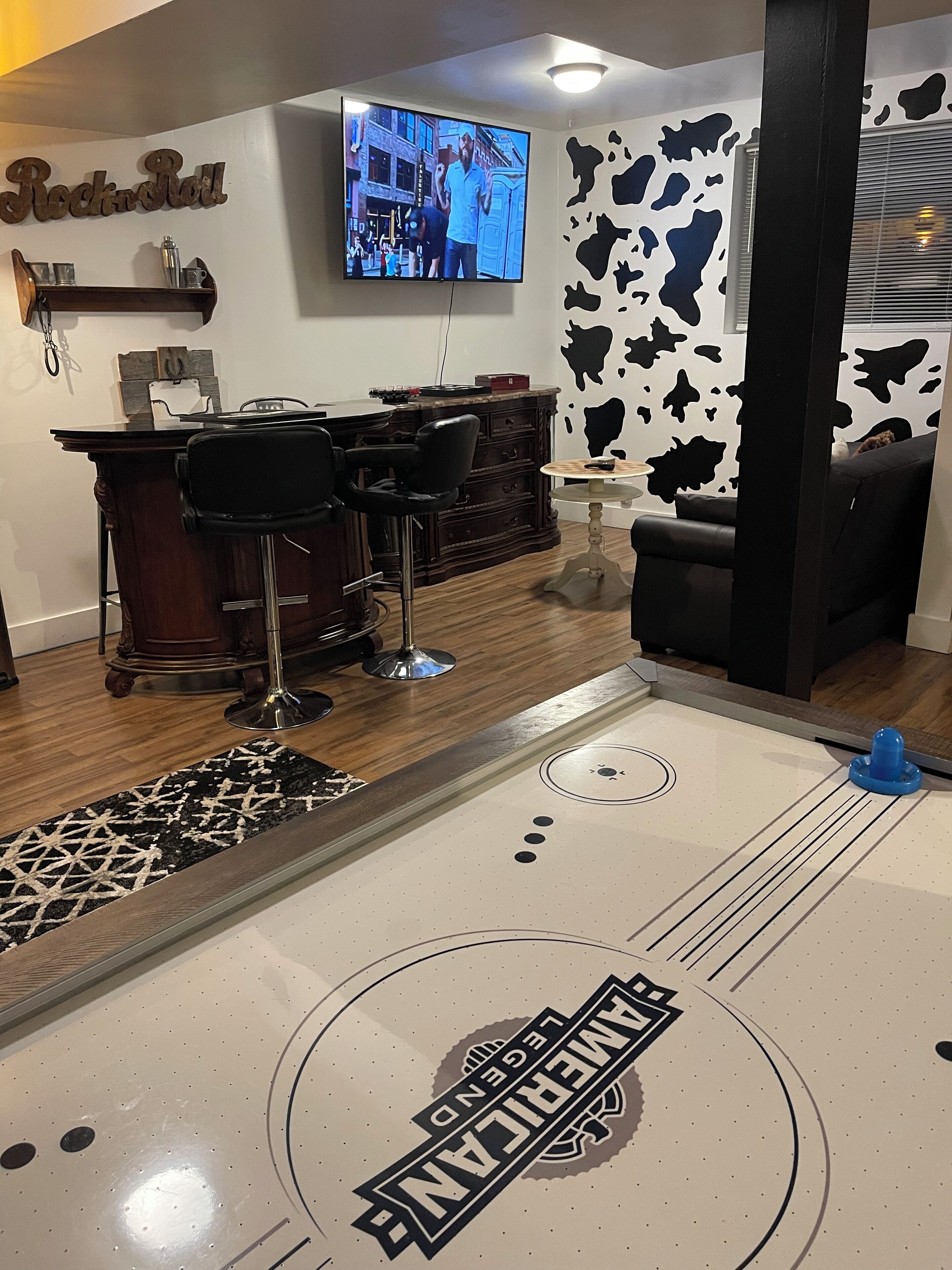 Zona de bar con televisor, taburetes, mostrador y pared con diseño de vaca.