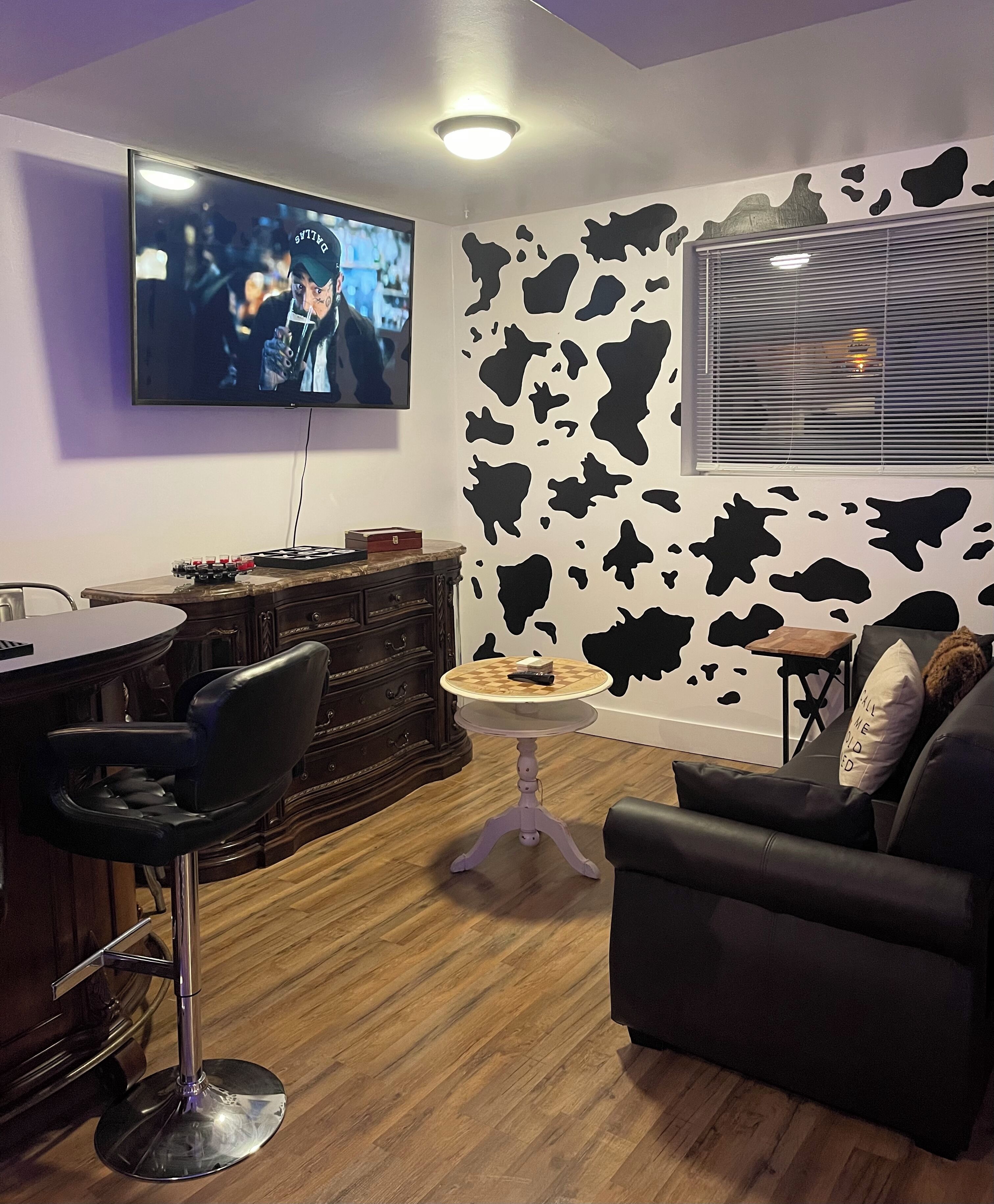 Una sala de estar moderna con una zona de bar, un televisor montado en la pared y un diseño de pared con estampado de vaca.