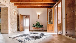 Un pasillo con pared de piedra, vigas de madera en el techo, un banco con plantas y una alfombra estampada.