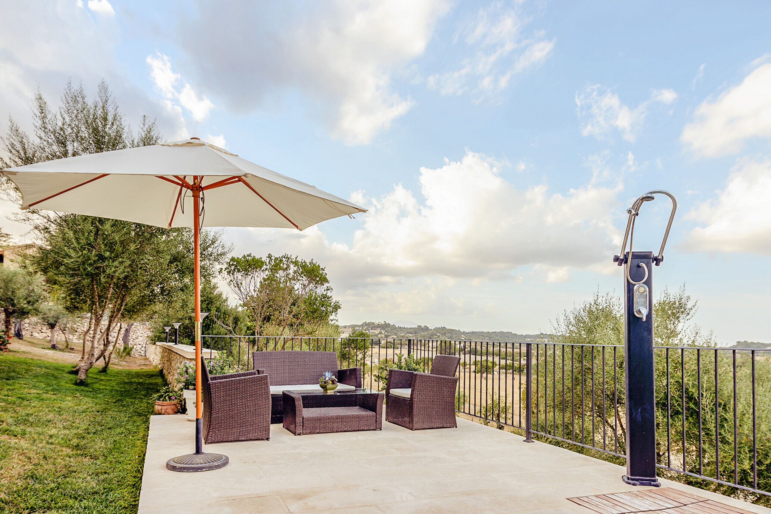 An outdoor patio with wicker furniture, a large umbrella, and a metal railing.