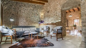 Una habitación rústica con paredes de piedra, un sofá, sillas, un tapete de cuero y una mesa con sillas.