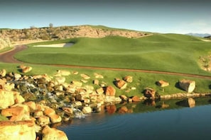 Un parcours de golf avec un étang, des rochers et un ciel dégagé.