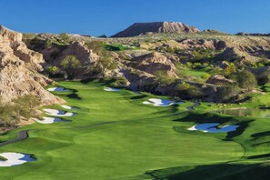 Un parcours de golf doté de bunkers, d’obstacles d’eau et offrant une vue imprenable sur un paysage montagneux.
