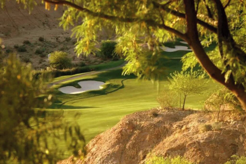 Campo de golf con un obstáculo acuático, árboles y un afloramiento rocoso.