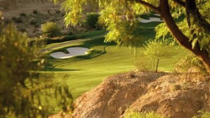 Campo de golf con un obstáculo acuático, árboles y un afloramiento rocoso.