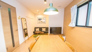 A modern room with a wooden dining table, a sofa with cushions, a TV, and a large window with curtains. - LA-CHIC Stay Hakata Ⅰ (Fukuoka)
