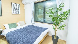 A bedroom with a bed, a potted plant, a window with curtains, and a wall-mounted air conditioner. - LA-CHIC Stay Hakata Ⅰ (Fukuoka)