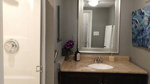 A bathroom with a white shower, a sink with a beige countertop, a dark wooden cabinet, a large mirror, and a purple flower vase. - Charming 3 bdr. Condo in Central Raleigh (Raleigh)