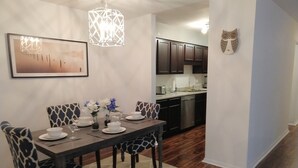 A dining area with a dark wooden table set for four, surrounded by patterned chairs. A modern pendant light hangs above, and a framed artwork is on the wall. - Charming 3 bdr. Condo in Central Raleigh (Raleigh)