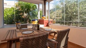 Uma sala de jantar com mesa posta para quatro pessoas, cadeiras de vime e vista para áreas verdes e edifícios através de grandes janelas.