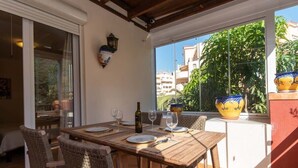 Uma sala de jantar com mesa de madeira e cadeiras de vime, uma garrafa de vinho e um vaso no parapeito da janela.