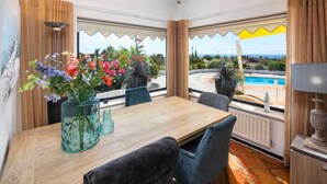 A dining area with a wooden table, chairs, and a view of a swimming pool and landscape. - Villa with pool and sea view.  Quiet location, beach and restaurants nearby. (Carvoeiro)