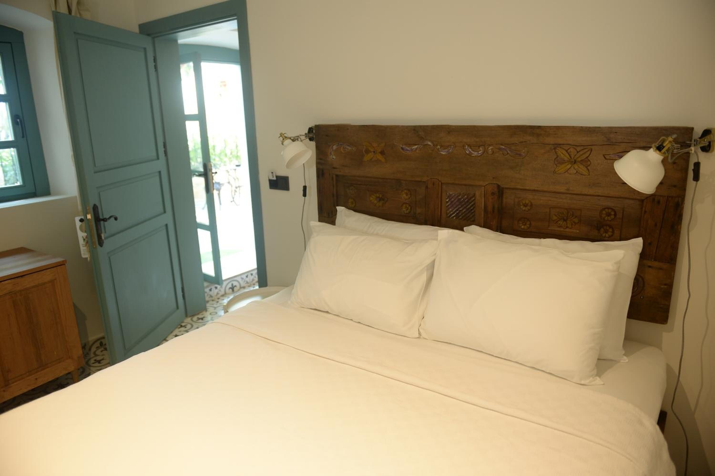 A bedroom with a wooden headboard, white bedding, a bedside lamp, and a door leading to a balcony.