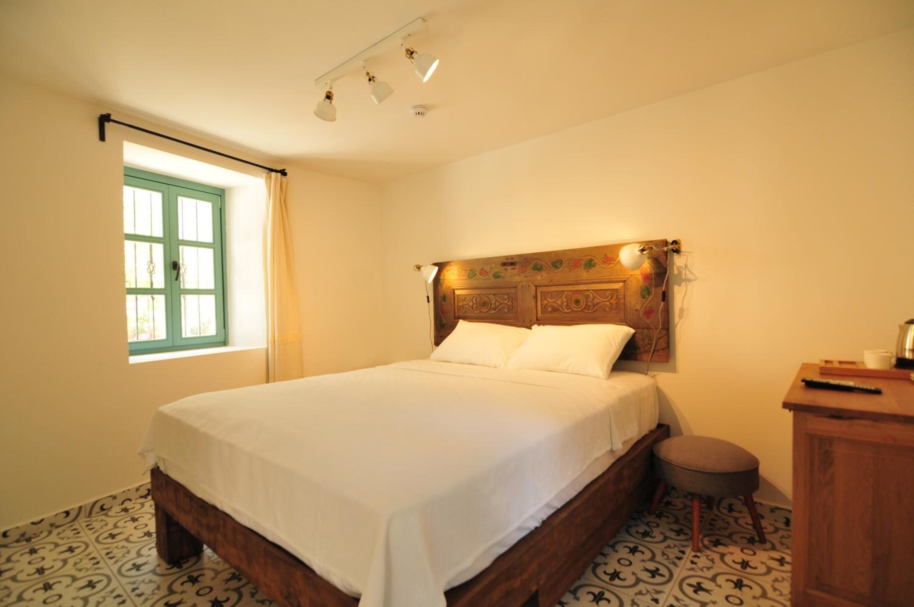 Una cama bien hecha con cabecera de madera, una mesita de noche pequeña y una ventana con cortinas.