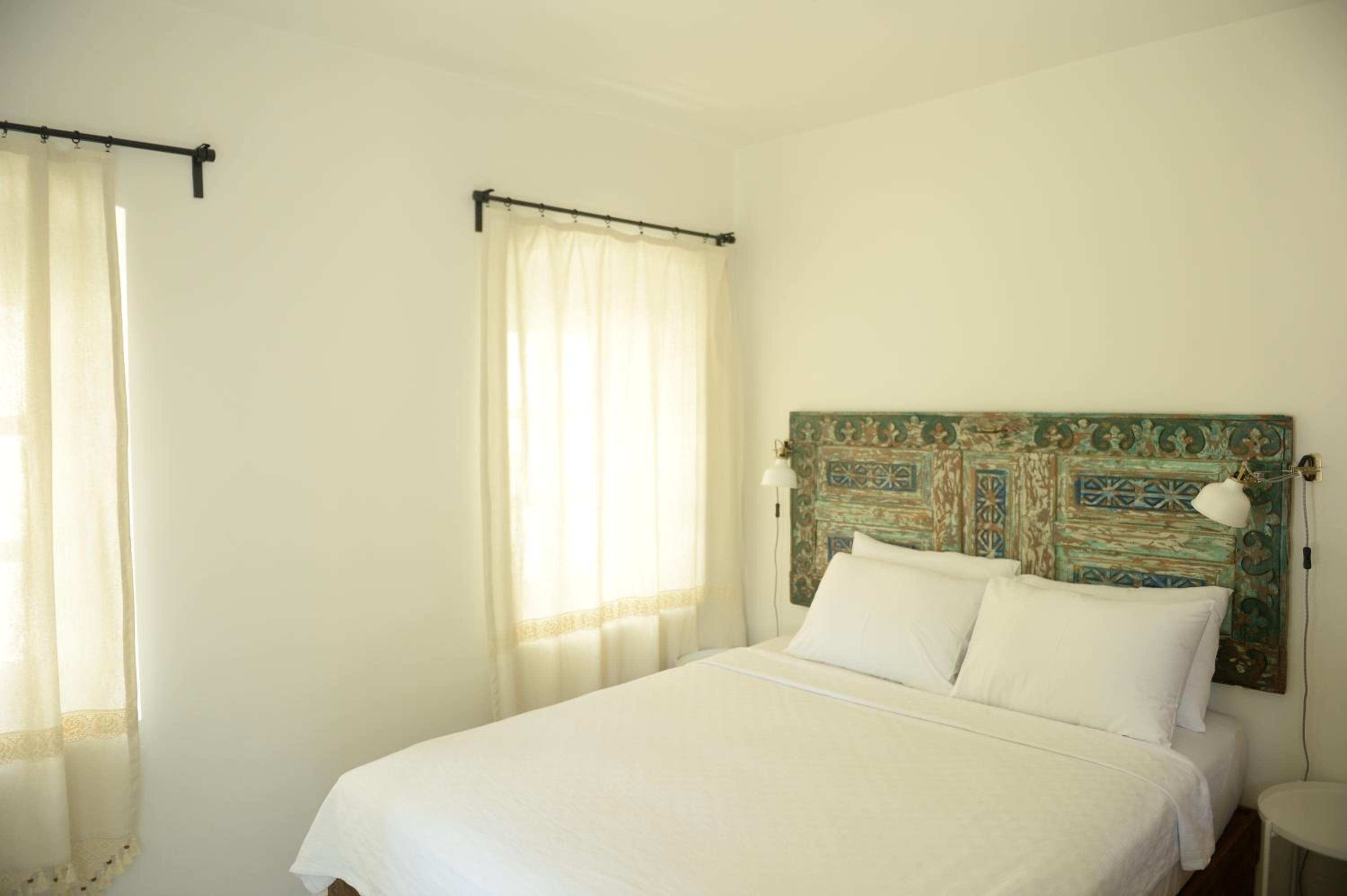 Une chambre à coucher avec un lit, des rideaux, une tête de lit avec une lampe et une petite table.