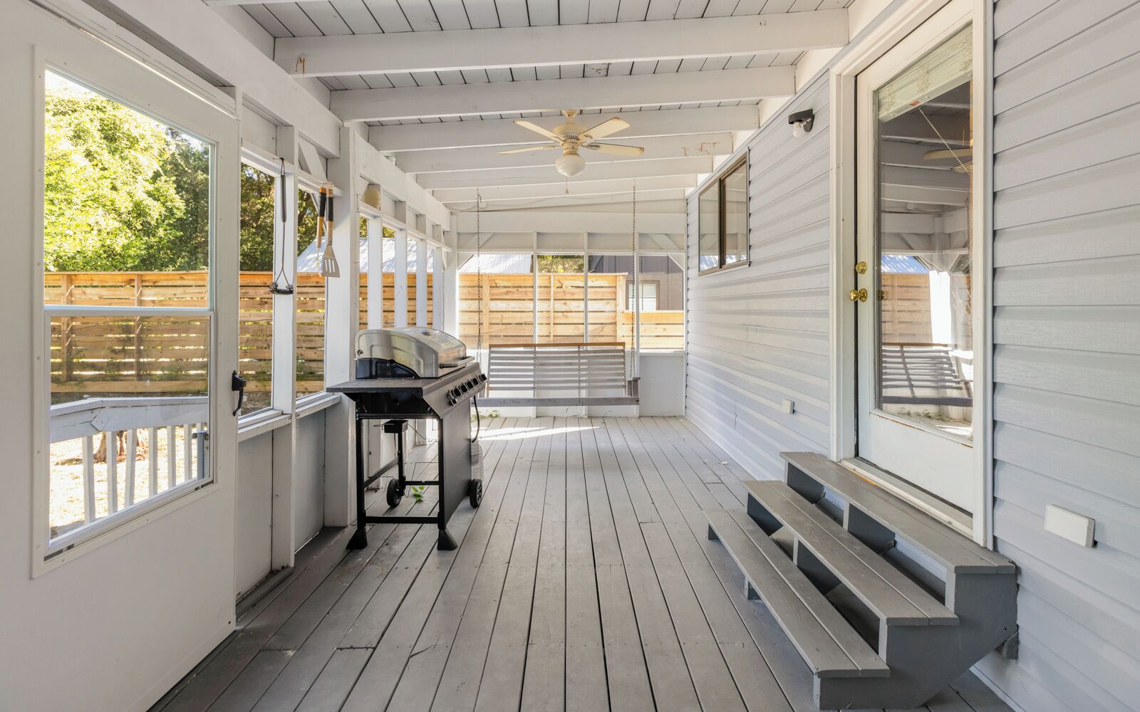 A covered porch with a grill, wooden steps, and a ceiling fan.