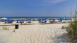 Ein Strand mit Reihen blauer Sonnenschirme und Liegen, feiner Sand und das Meer im Hintergrund.