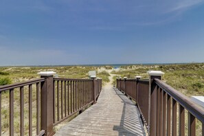 A wooden boardwalk leading to the beach, surrounded by dunes and clear skies.