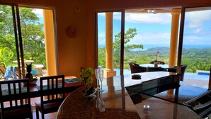 A dining area with a view of the ocean, featuring a round table, chairs, and a potted plant. - Stunning 180 degree Ocean, Mountain and Jungle Views! (Ojochal)