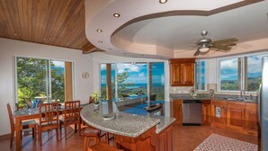 A modern kitchen with a central island, wooden cabinets, and large windows offering ocean views. - Stunning 180 degree Ocean, Mountain and Jungle Views! (Ojochal)