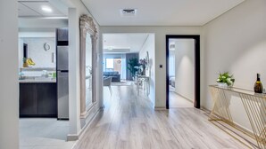 Una cocina moderna con un refrigerador de acero inoxidable, una zona de comedor con una mesa de vidrio y un pasillo que conduce a una sala de estar.