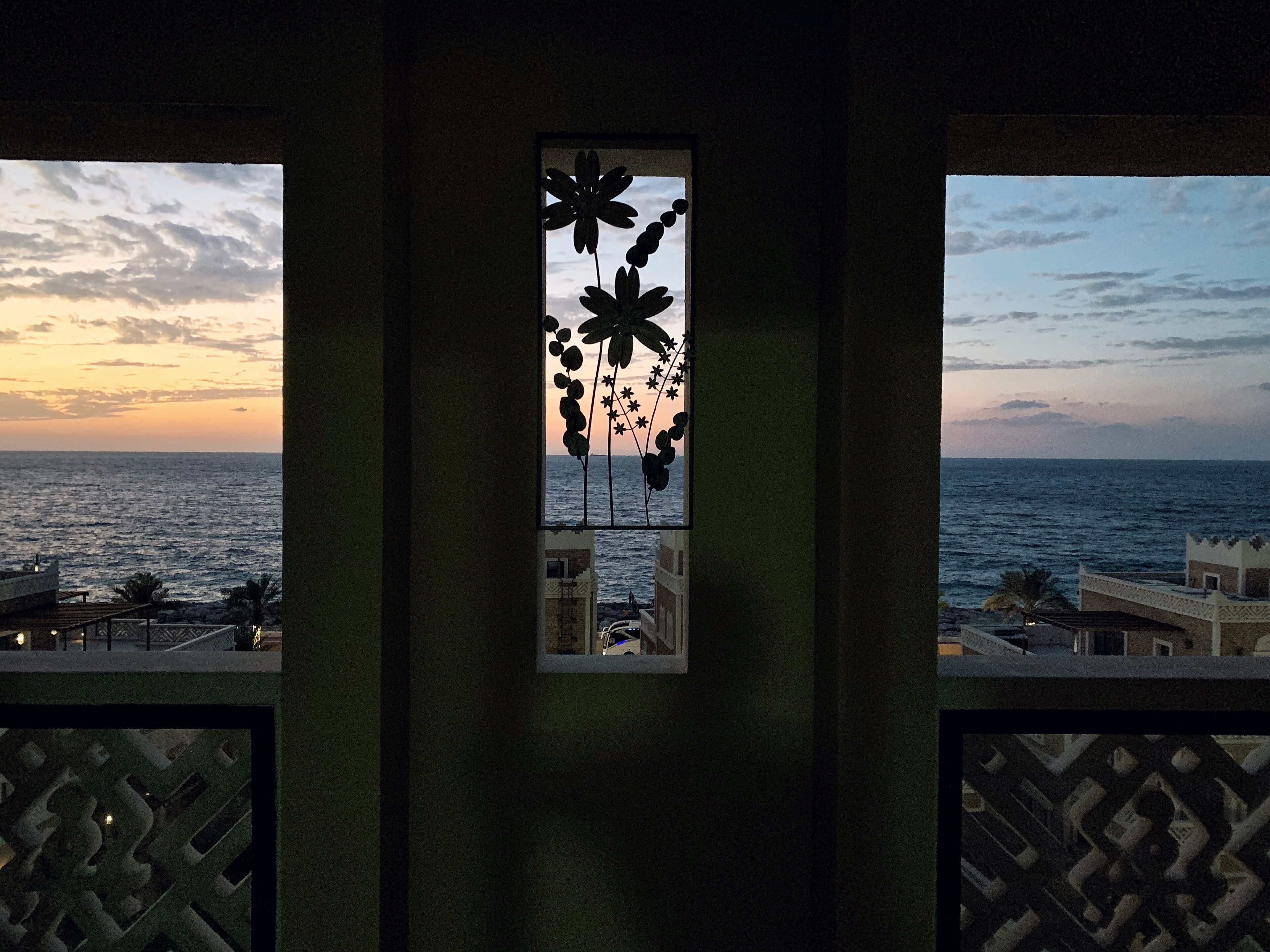 A balcony with a view of the sea at sunset, featuring a decorative window with floral patterns.