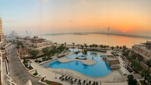Un resort con una amplia piscina, palmeras y vistas a un horizonte urbano al atardecer.