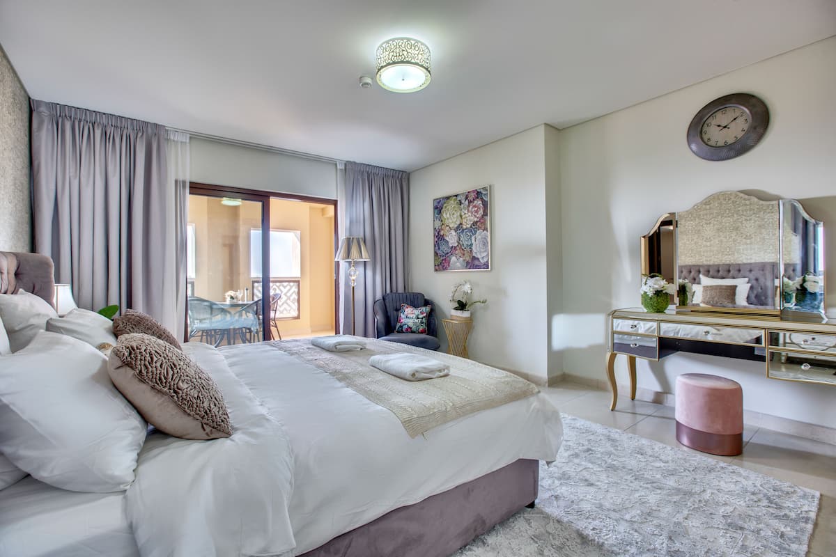 Une chambre élégamment aménagée, dotée d’un grand lit, d’une coiffeuse avec miroir et offrant une vue sur l’extérieur.