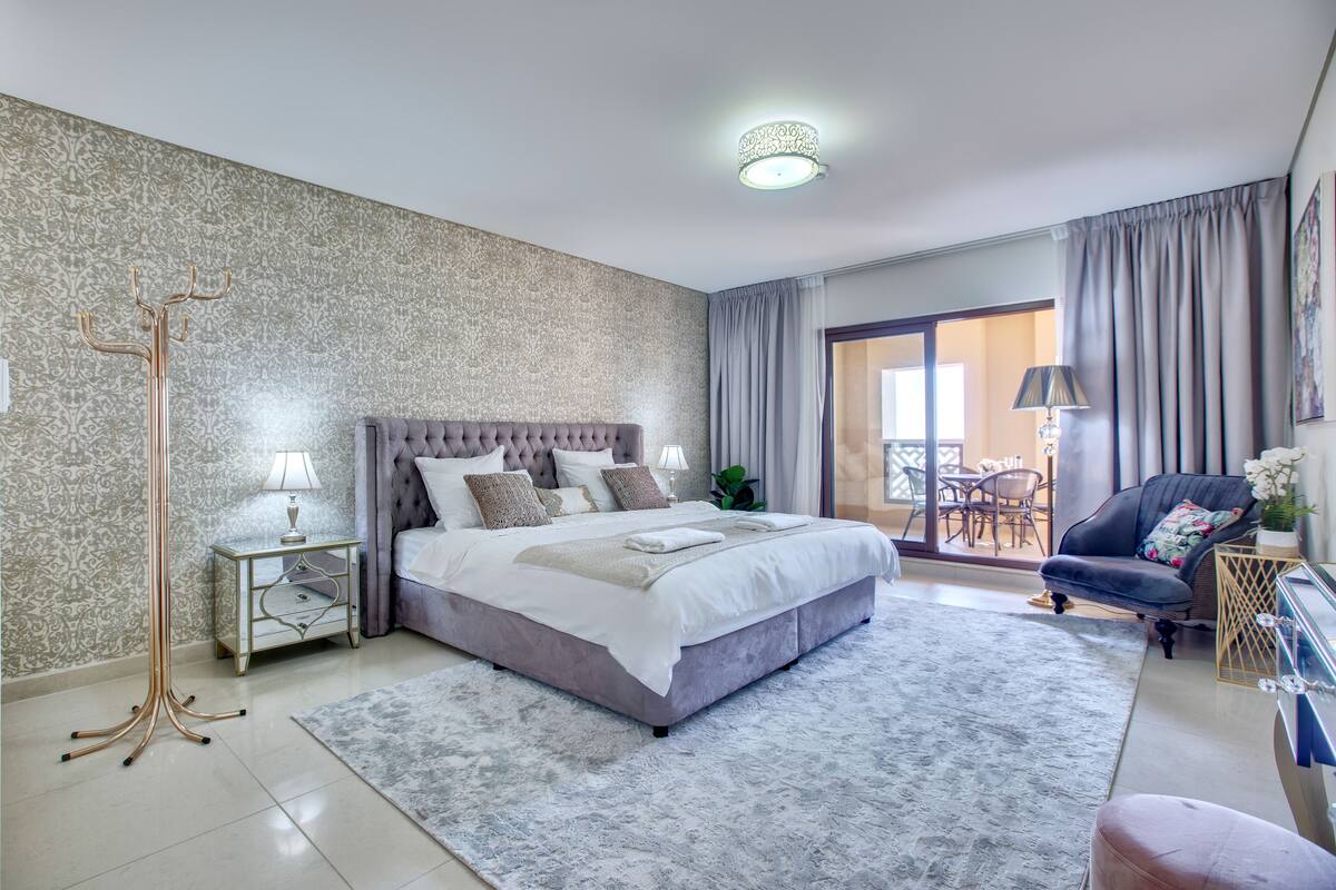 Une chambre moderne avec un grand lit, une table de chevet avec une lampe, un lampadaire et une vue sur la terrasse extérieure.