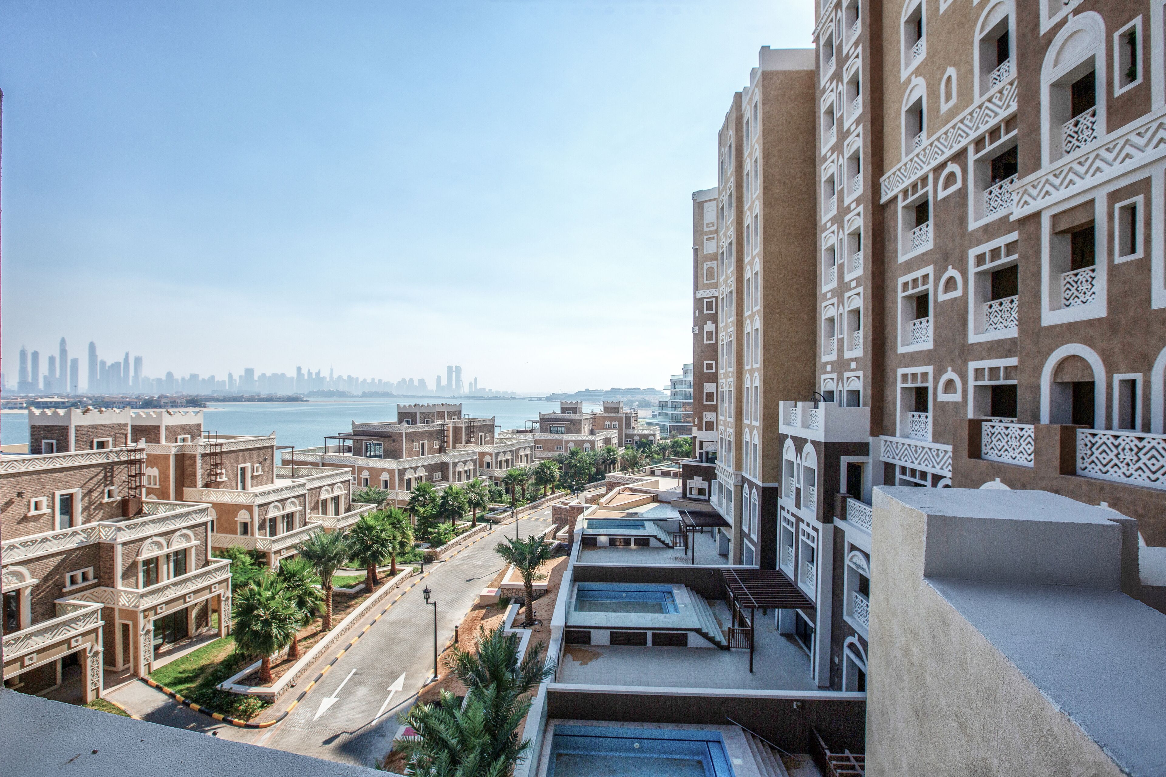 A residential area with traditional architecture, a clear view of the sea, and a distant city skyline.