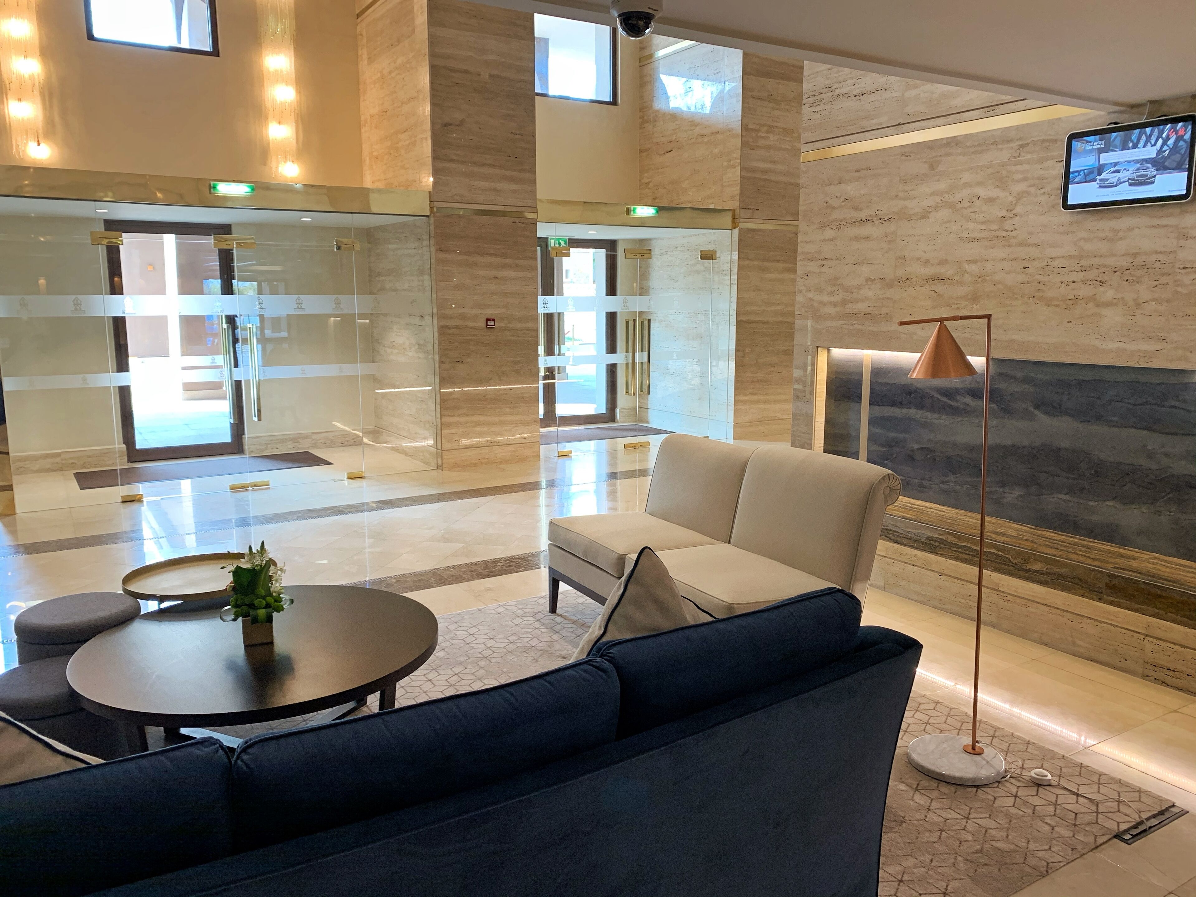 A spacious lobby with a modern design, featuring a sofa, a round table with a vase, and a floor lamp.