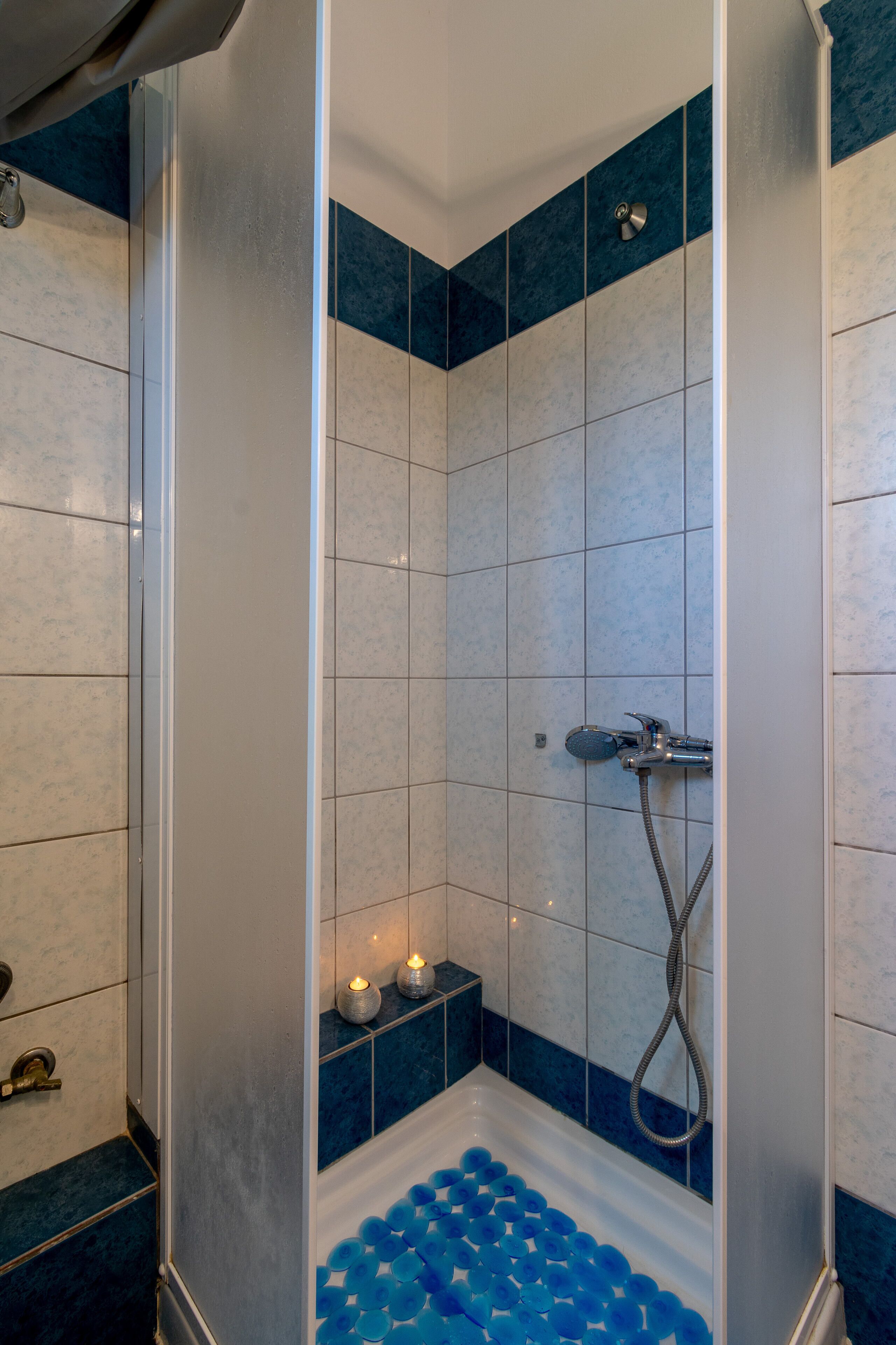 Een douche met blauwe tegels, een handdouche en een badkuip gevuld met blauwe badbommen.