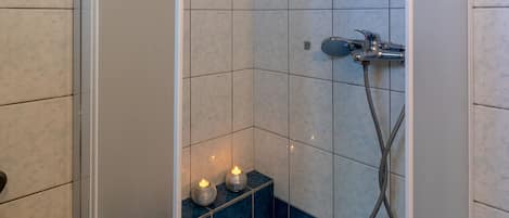 Een douche met blauwe tegels, een handdouche en een badkuip gevuld met blauwe badbommen.