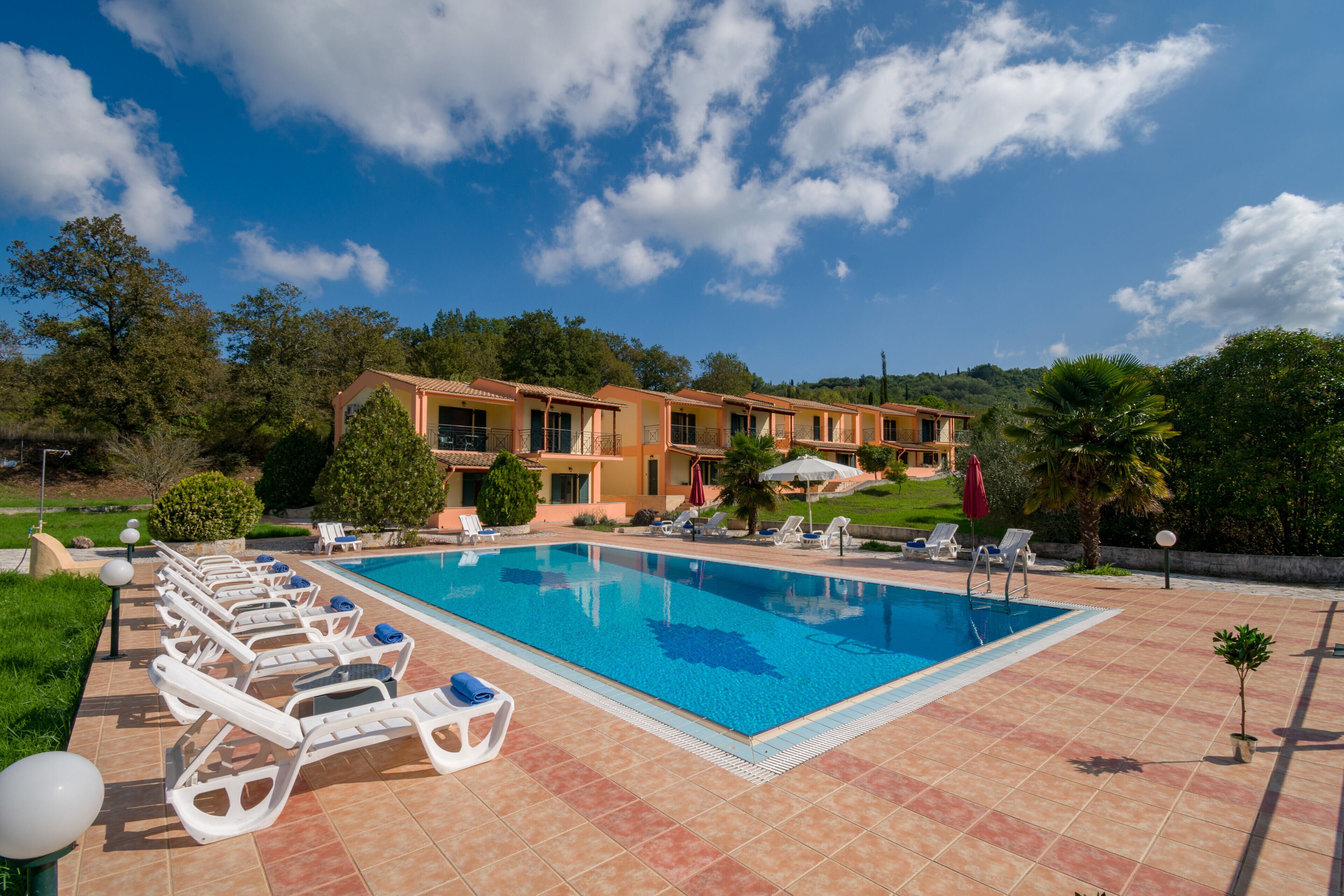 A swimming pool with lounge chairs and umbrellas, surrounded by a building with multiple balconies.