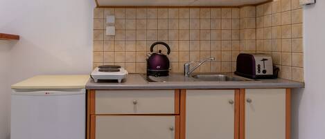 Una cocina compacta con armarios color crema, un refrigerador pequeño, un hervidor, un tostador y un lavamanos.