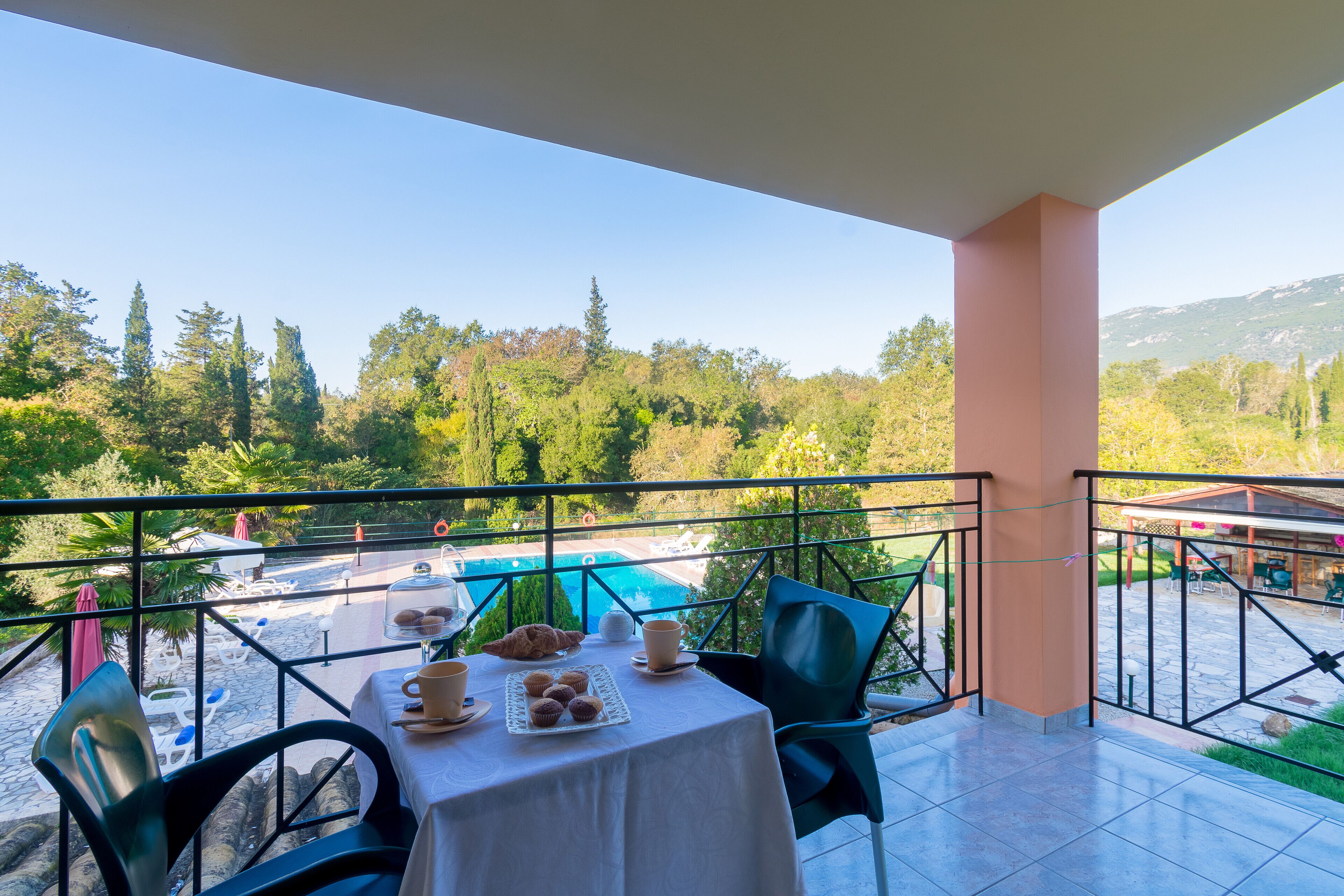 A balcony with a table set for breakfast, overlooking a pool and lush greenery.