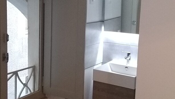 Une petite salle de bain étroite, avec un miroir, un lavabo et une douche.