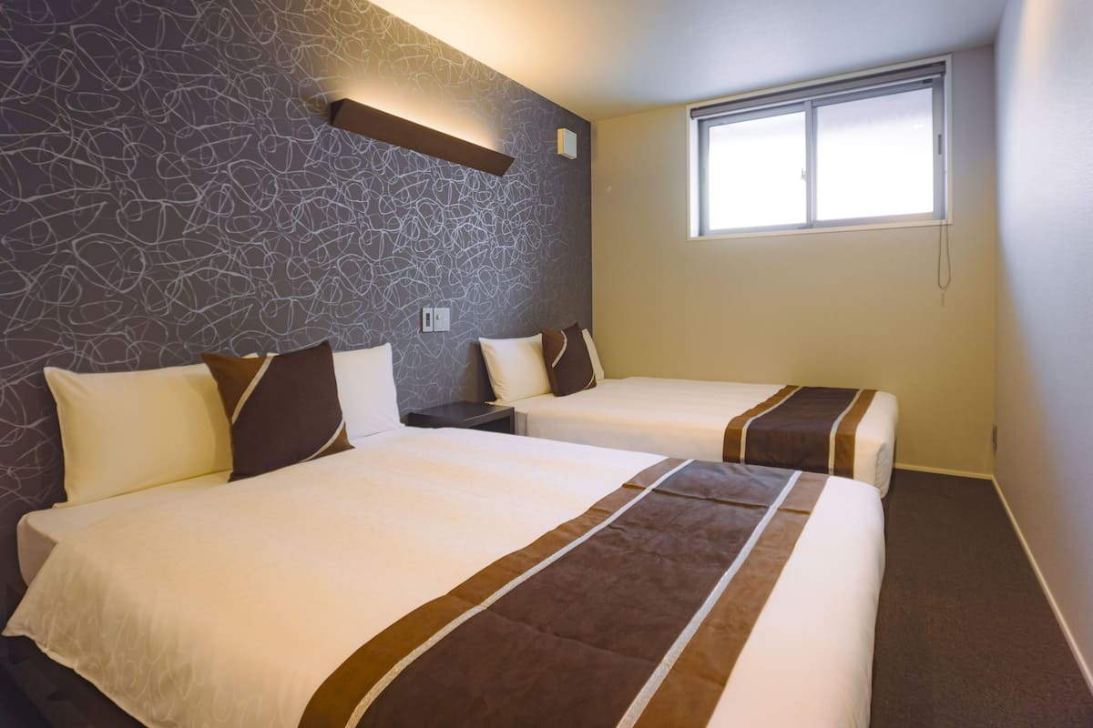 A hotel room with two beds, a stone-patterned wall, a window, and a nightstand.