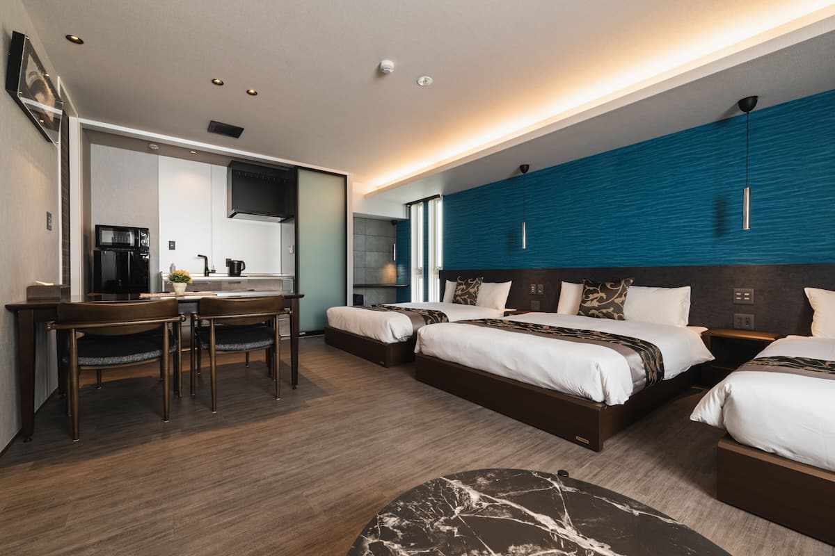 Quarto de hotel moderno com duas camas, área de refeições e cozinha compacta.
