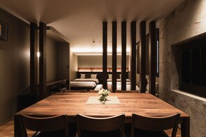 A spacious dining area with a wooden table and chairs, a small vase with flowers, and a view of a bedroom with a bed and a nightstand.