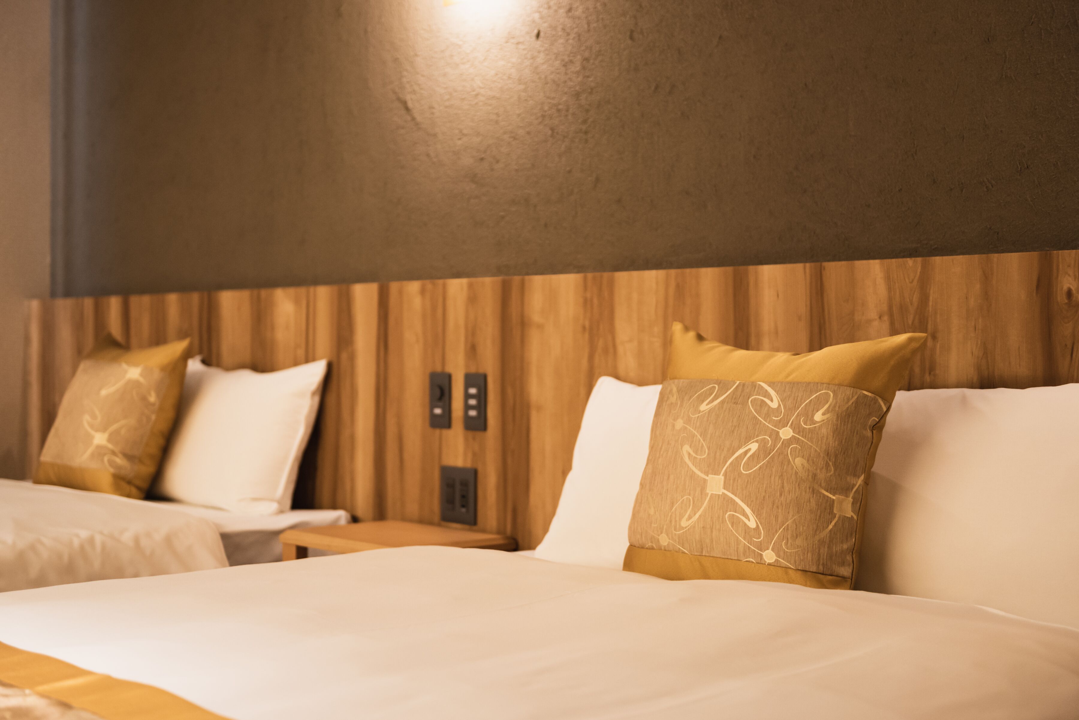 Hotellihuone, jossa on kaksi sänkyä, puinen pääty ja seinässä oleva ohjauspaneeli.