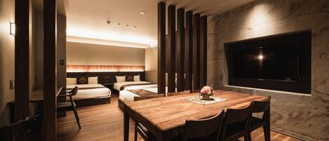 A modern hotel room with a wooden dining table, two beds, a TV, and a large window.