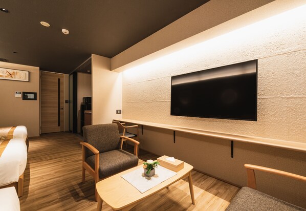 A hotel room with a bed, a desk with a vase, a chair, and a TV mounted on the wall.