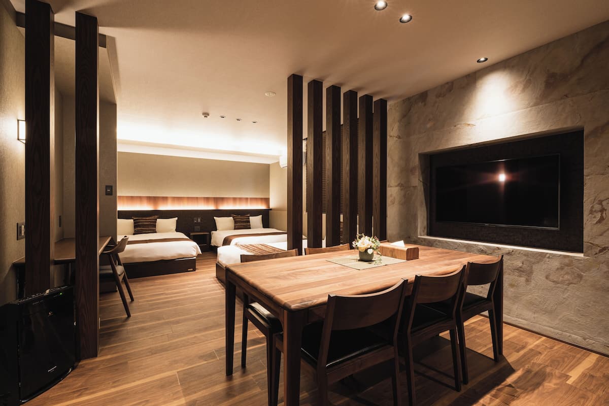 Quarto de hotel moderno com uma mesa de jantar de madeira, duas camas, uma TV e uma parede de pedra.