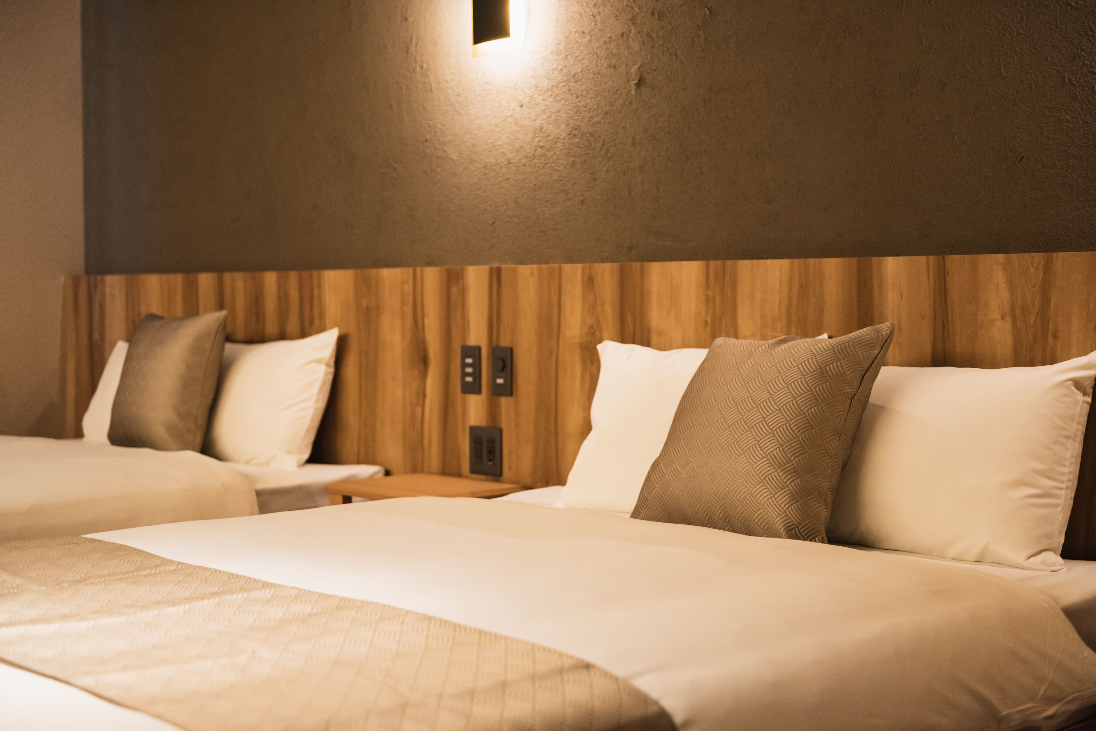 A hotel room with two beds, wooden headboard, and a small wall-mounted light fixture.