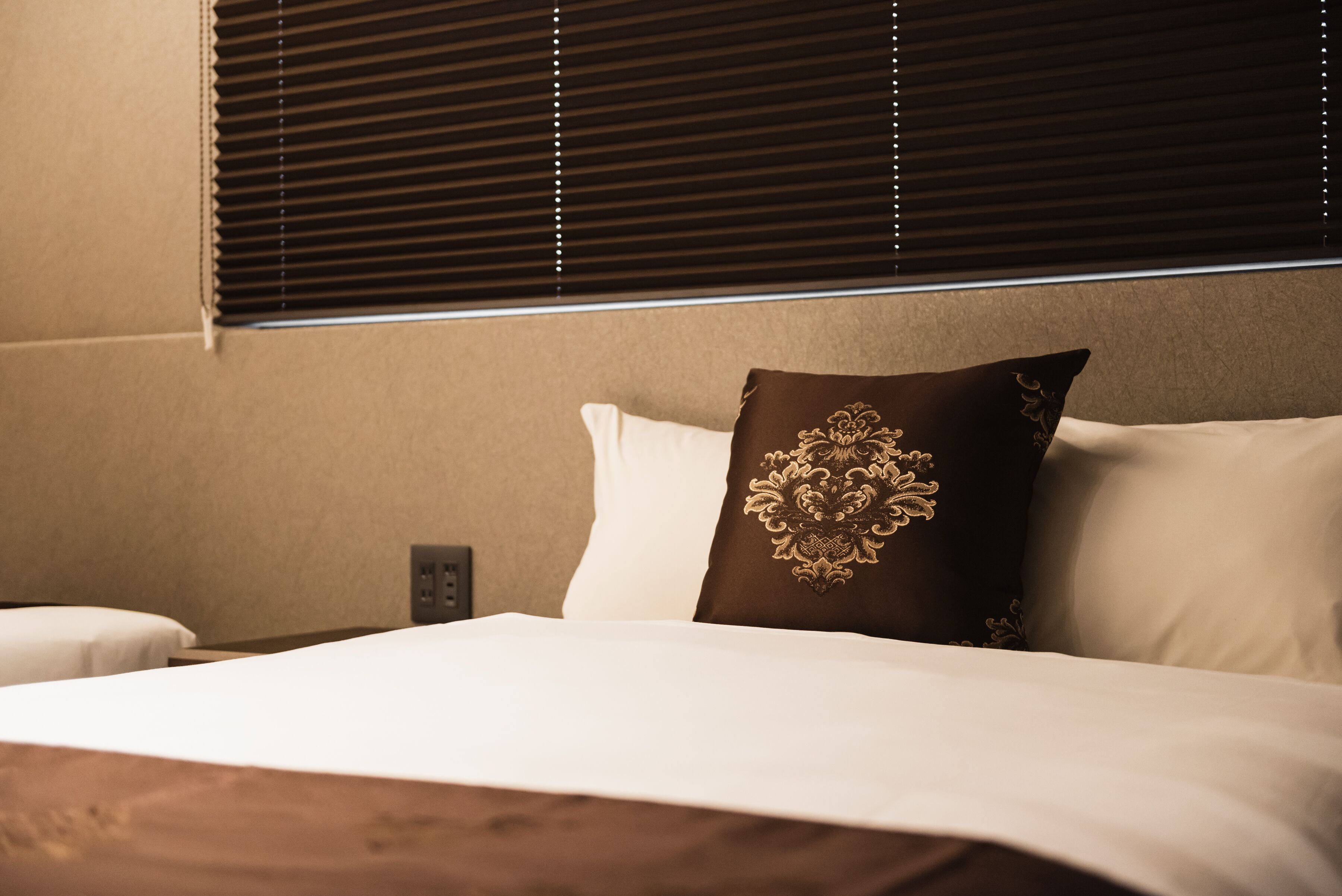 A hotel room with a bed, a nightstand, and a wall socket.